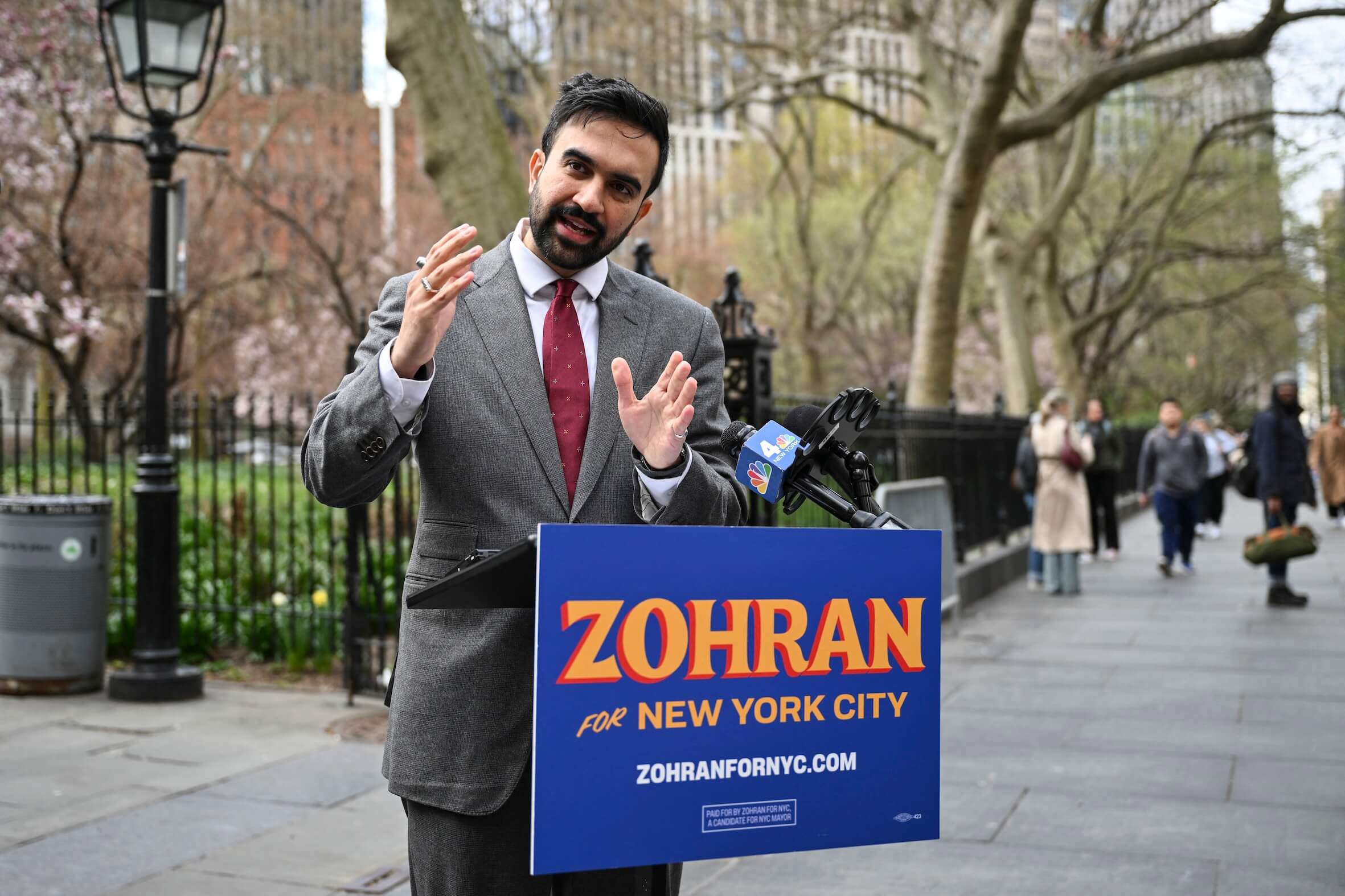 Zohran Mamdani will Spenden an Israel verbieten und unterstellte der Polizei Rassismus. Auf dem Rednerpult steht sein Slogan: „For New York City“