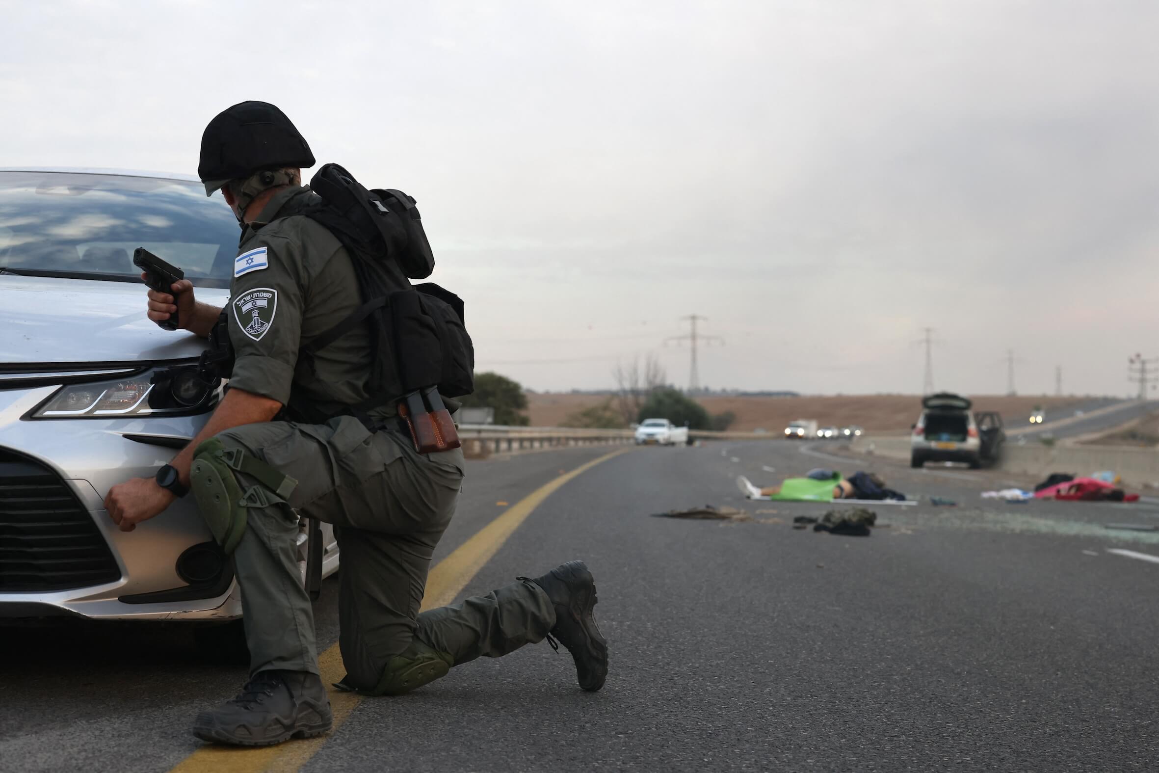 Ein israelischer Soldat geht hinter einem Auto in Deckung. Dabei blickt er auf Leichen auf einer Hauptstraße in der Nähe des Kibbuz Gevim nahe der Grenze zu Gaza.